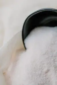 Detailed close-up of Himalayan bath salt spilling from a black scoop, symbolizing self-care.